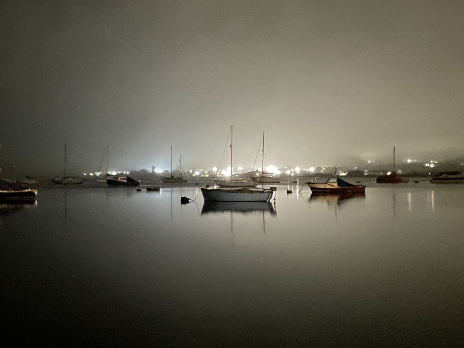 Boats resting in a misty harbour, lights reflected on still water