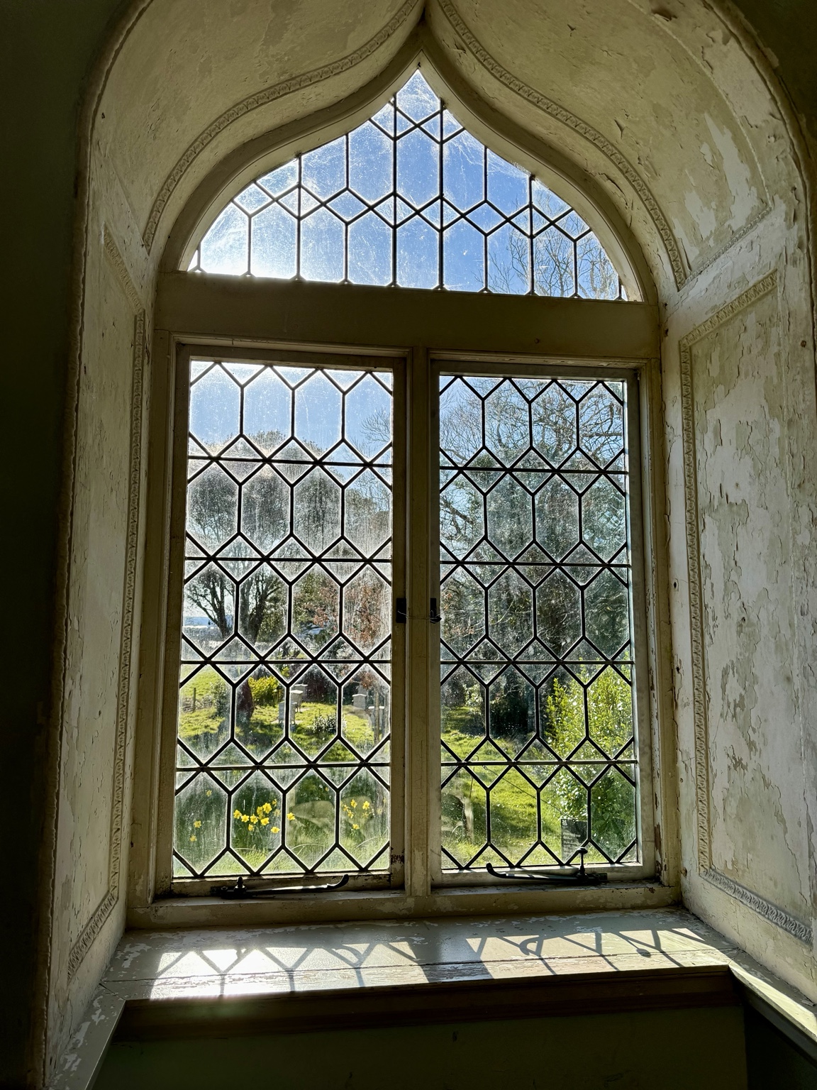 An old arched window opening a view onto trees and daylight